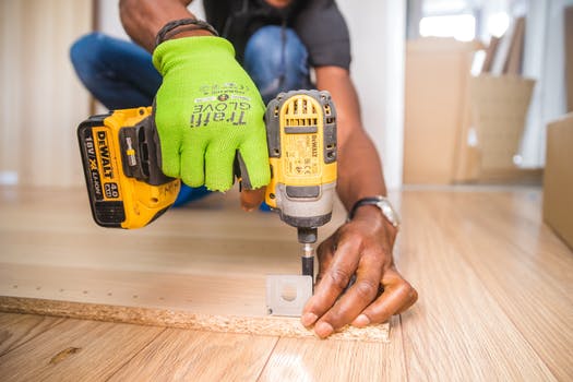 Close up of a modern joiner tool being used on wood by a lime green glove covered hand.